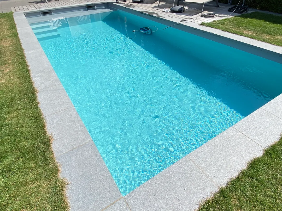 Modern ingegraven zwembad met lichtblauw water en grijze natuurstenen boord
