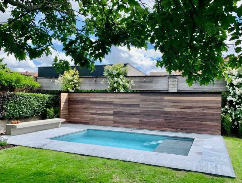 Modern zwembad met nieuwe lichtblauwe liner, strakke grijze tegels en houten accentwand in een groene tuin