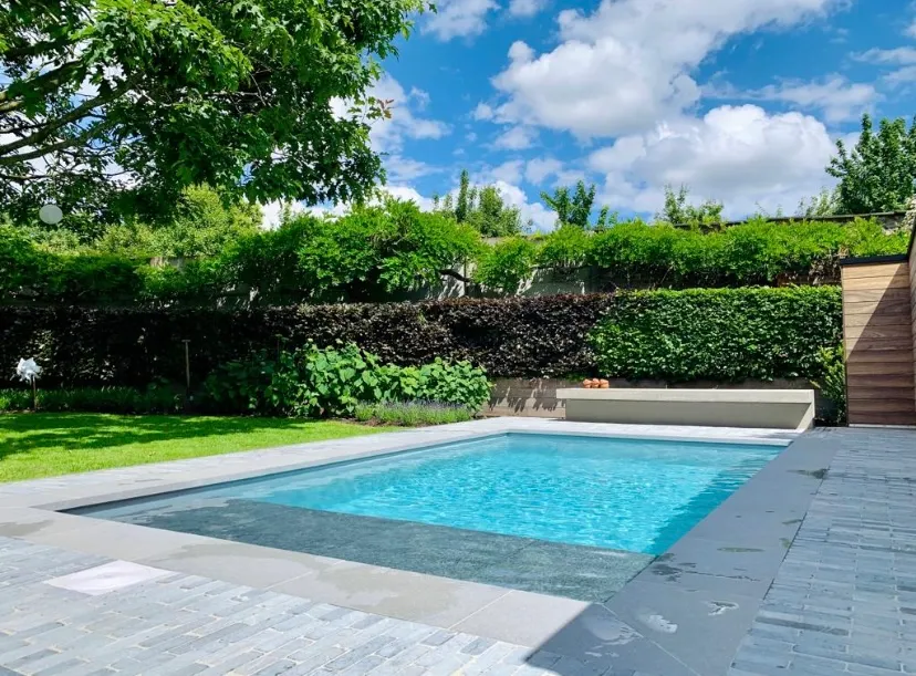 Modern zwembad met strak geplaatste blauwe liner en professionele afwerking in een groene tuin