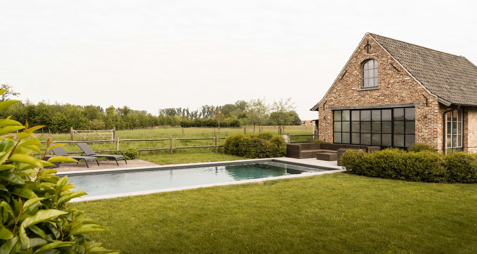 Grijze zwembadliner met lichte boord bij een bakstenen poolhouse en lounge in West-Vlaanderen — renovatie door Liner Plaatsen